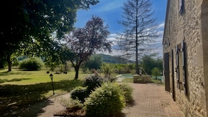 A paved pathway leading to a building with a stone facade, surrounded by lush greenery and trees.