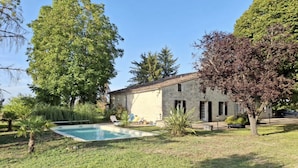A stone building with a swimming pool, surrounded by trees and grass.
