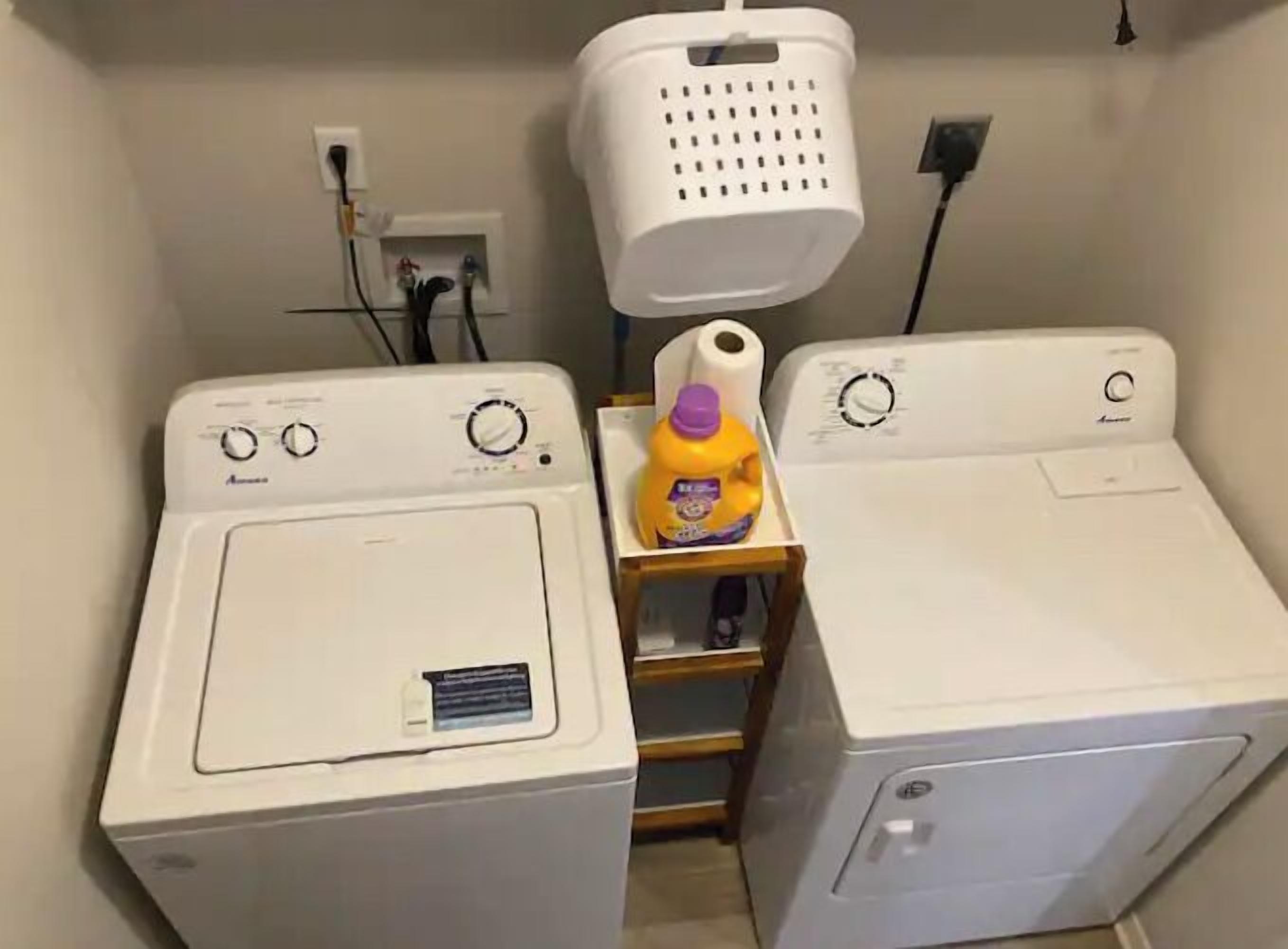 Un área de lavandería con dos lavadoras de carga frontal, un tendedero y una botella de detergente.