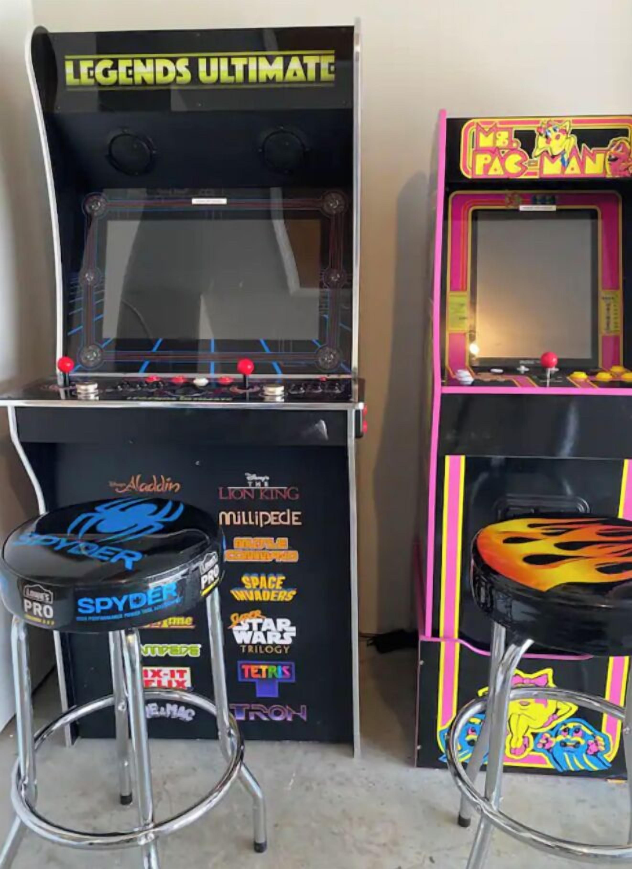 Two arcade machines, one labeled 'LEGENDS ULTIMATE' and the other 'PAC-MAN', with various game titles displayed on their sides.