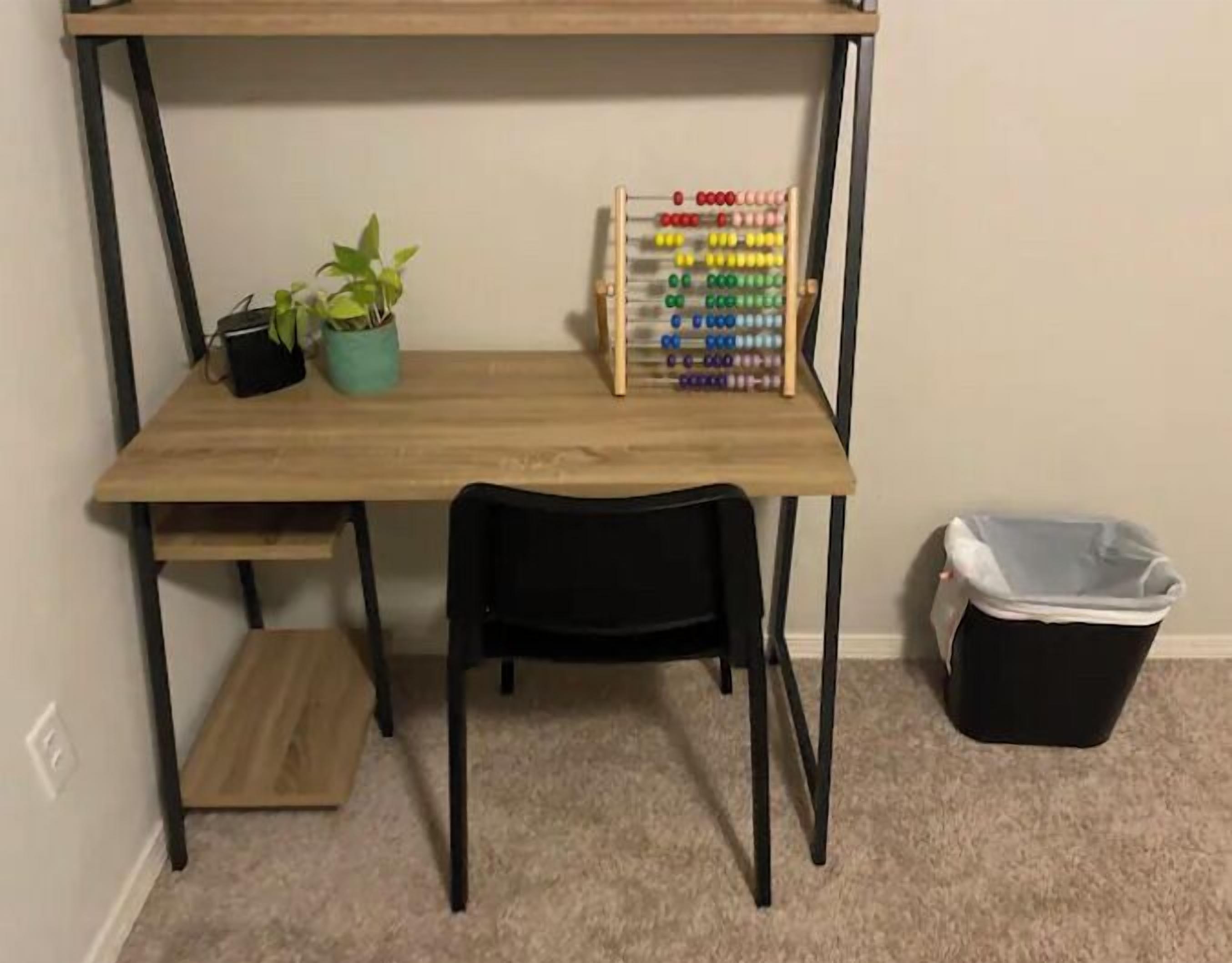 Een houten bureau met een zwarte stoel, een potplant en een rekenkader.