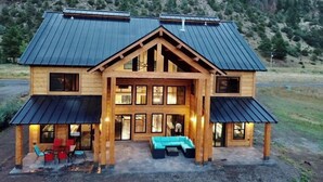 Une cabane en rondins avec un toit en métal, de grandes fenêtres et une véranda dotée de sièges pour l’extérieur.