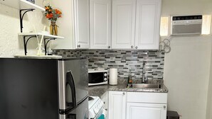 A compact kitchen with white cabinets, a stainless steel refrigerator, a microwave, and a sink with a tiled backsplash.