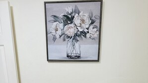 A dining table set with plates, glasses, and cutlery, with a framed floral artwork above it.
