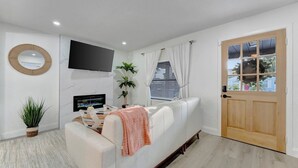 Ein modernes Wohnzimmer mit einem weißen Sofa, einem an der Wand befestigten Flachbildfernseher, einem Kamin und einer Holztür.