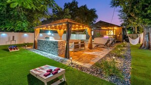 Ein Garten mit einer hölzernen Pergola, einem Steinofen und einer Sitzgruppe im Freien.