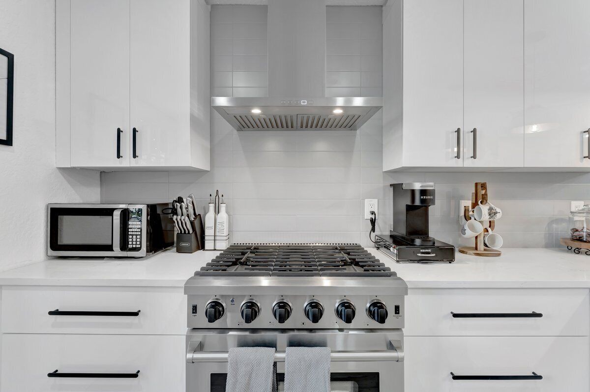 A modern kitchen with white cabinets, a built-in microwave, a gas stove, and a coffee maker.