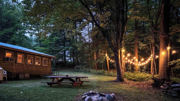 Een rustiek vakantiehuisje met een picknicktafel en een vuurkuil in een bebost gebied.