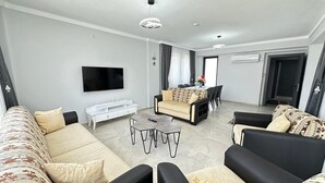 A modern living room with a sofa set, a coffee table, a TV mounted on the wall, and a dining area with chairs and a table. - Safe, central, lux and comfortable holiday in Dalyan. (Dalyan)