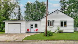 Ein bungalow mit Garage, zwei rote Stühle draußen und einem gepflegten Rasen.