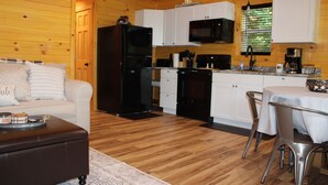 A compact kitchen with white cabinets, a black refrigerator, and a microwave. There's a dining area with a table and chairs, and a sofa with a tray on it.