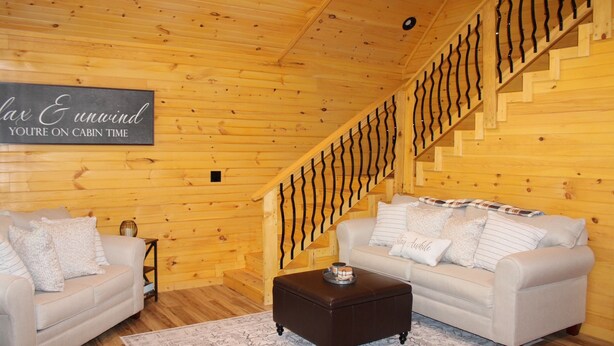 A cabin interior with two sofas, a coffee table, a staircase with a unique railing, and a sign on the wall.