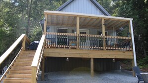 A two-story wooden cabin with a covered deck and a staircase leading to the upper level.