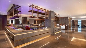 A modern hotel lobby with a central reception desk, a staircase with a wooden railing, and a bar area with a counter and stools. - Ramada by Wyndham Taizhou West (Taizhou)