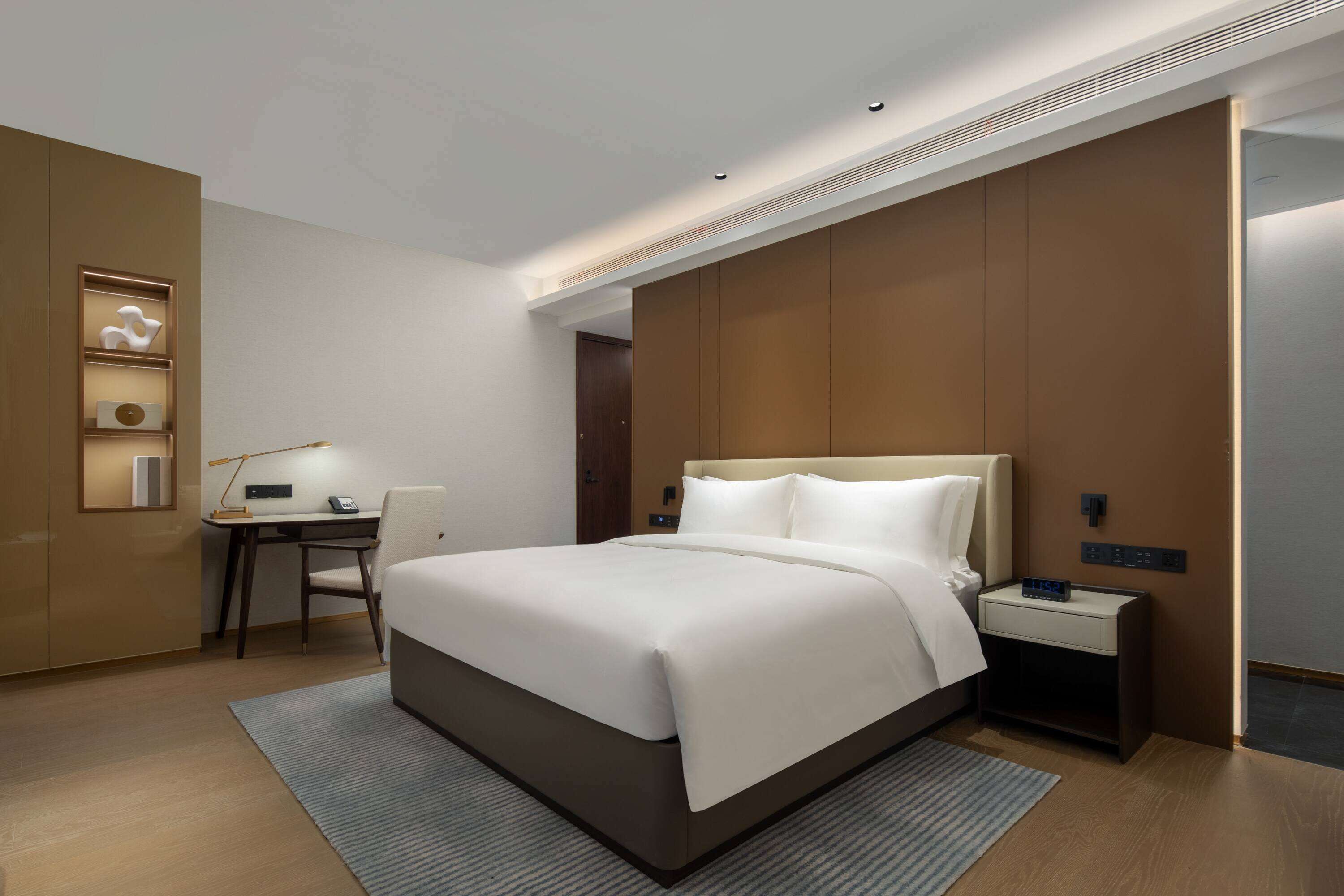 A modern hotel room with a large bed, a desk, and a nightstand.