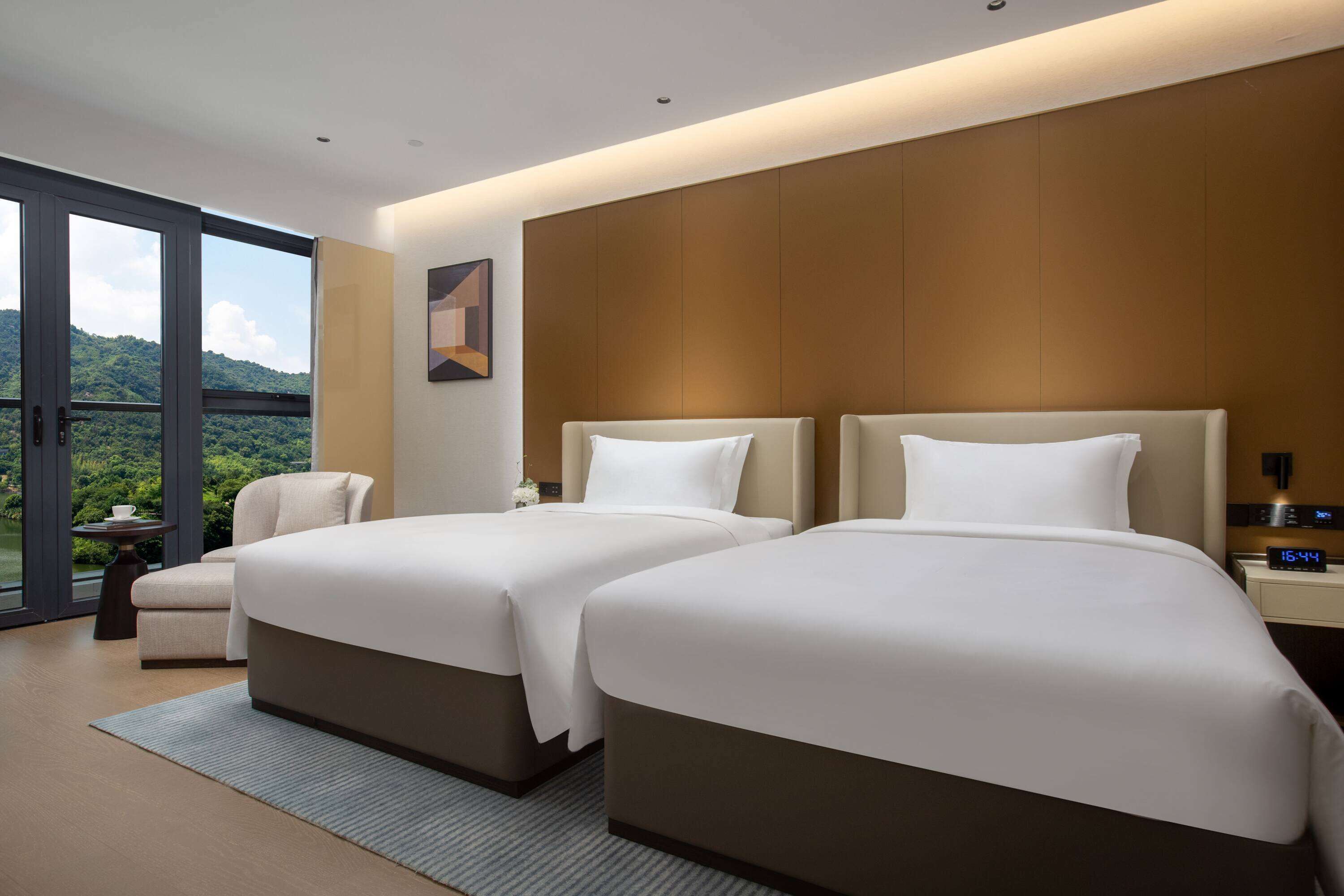 Habitación de hotel con dos camas, vistas a un paisaje montañoso y un pequeño rincón de descanso.