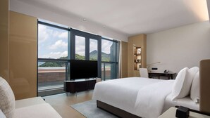 A hotel room with a large bed, a TV, a desk, and a view of mountains through large windows. - Ramada by Wyndham Taizhou West (Taizhou)