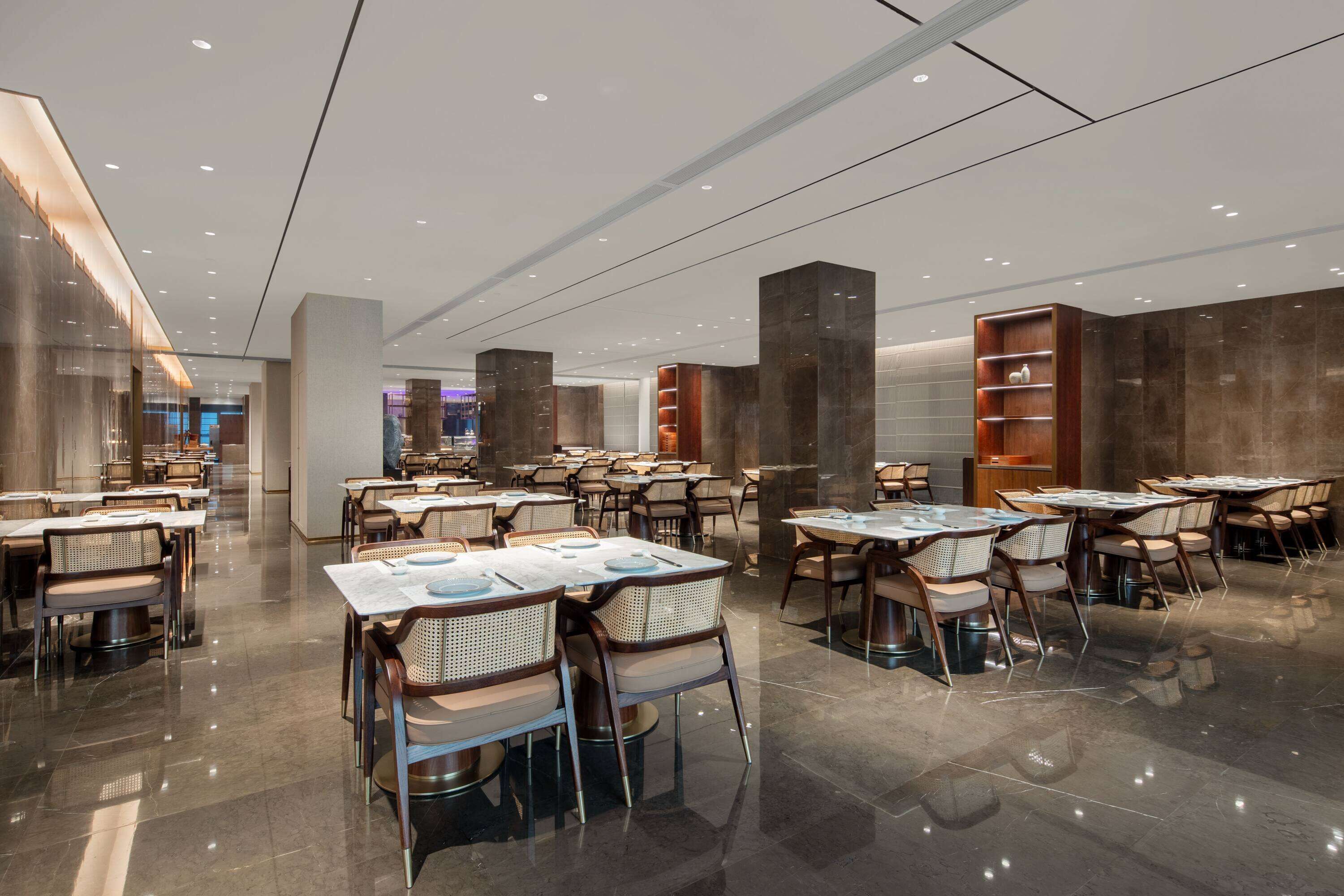 A modern restaurant with multiple tables and chairs, a polished floor, and contemporary lighting fixtures.