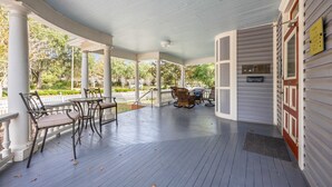 Een overdekt terras met een tafel en stoelen, een klein zitgedeelte en uitzicht op de groene omgeving.