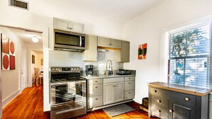 Een moderne keuken met roestvrijstalen apparatuur, houten vloeren en een raam met jaloezieën.