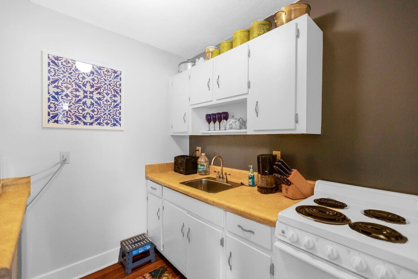 A compact kitchen with white cabinets, a wooden countertop, a sink, and a stove.