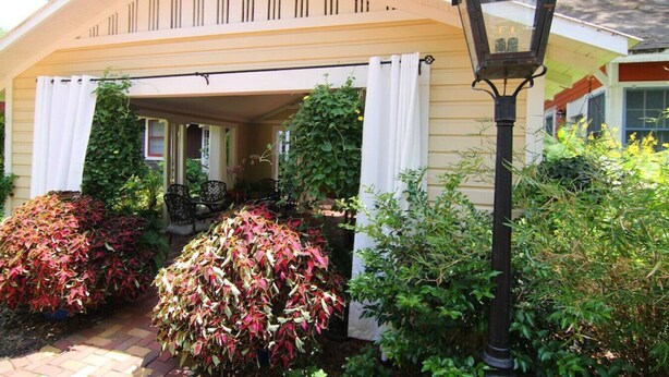 A covered porch with a bench, a lamp post, and various plants.