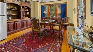 A dining area with a round table, chairs, a glass-top table, a red patterned rug, wooden cabinets, and a chandelier.