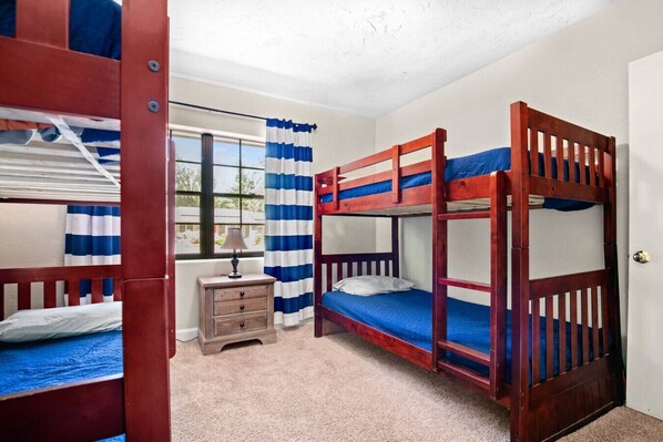 Una habitación con literas, una mesita de noche de madera, una lámpara y una ventana con cortinas.