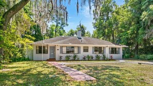 A single-story house with a front porch, surrounded by a well-maintained lawn and trees.