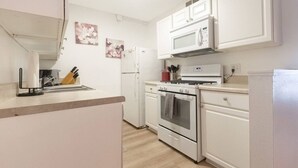 A kitchen with white cabinets, a microwave, a stove, and a refrigerator. - 1 Bedroom Condo: Walk to Shands / UF / VA- Pool! (Gainesville)