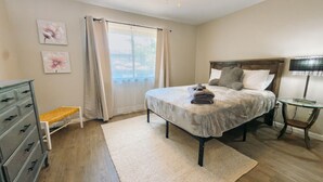 Un dormitorio con una cama, un aparador, un banco, una mesita de noche y un ventilador de techo.