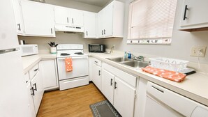 Una cocina con armarios blancos, un microondas, una estufa, un fregadero y un lavavajillas.