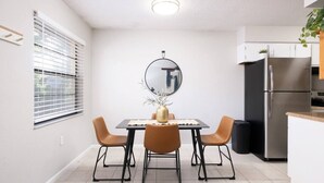 Une cuisine moderne équipée d’un réfrigérateur en acier inoxydable, d’une table à manger avec quatre chaises et d’un grand miroir placé au-dessus de la table.