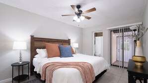 Une chambre à coucher avec un lit, des tables de chevet, un ventilateur de plafond et une vue sur l’extérieur.
