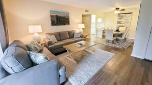 A modern living room with a sofa set, coffee table, and dining area with chairs and a table. - Large 1 BR Condo - Next to Oaks Mall and Hospital (Gainesville)
