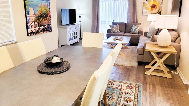 A modern living room with a dining area, a sofa set, a TV, and artwork on the walls. - Large 1 BR Condo - Next to Oaks Mall and Hospital (Gainesville)