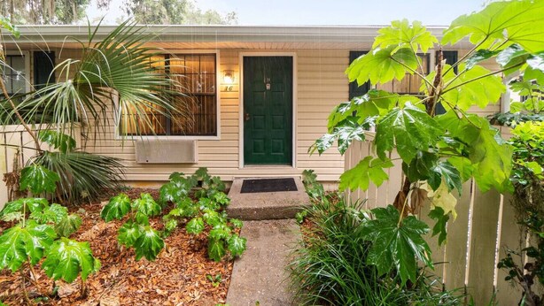 A single-story house with a green door, a small porch, and a garden with various plants.