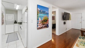 A modern kitchen with white appliances, a dining area with a wooden table, and a large scenic painting on the wall.