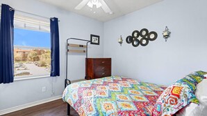 Ein Schlafzimmer mit einem Bett, einem Schminktisch, einem Fenster mit Vorhängen, einem Deckenventilator und Wandleuchten.