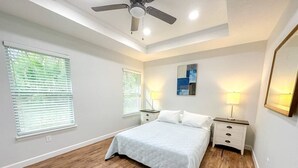 Ein Schlafzimmer mit einem Bett, zwei Nachttischen, einem Deckenventilator und einem Fenster mit Jalousien.