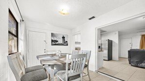 A dining area with a wooden table and white chairs, a kitchen with a refrigerator, and a view of a building outside. - Downtown Duplex- Spacious and Comfy 2 Bedroom (Gainesville)