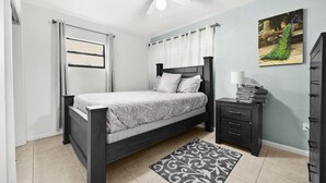 A bedroom with a bed, a nightstand, a dresser, a ceiling fan, and a painting on the wall. - Downtown Duplex- Spacious and Comfy 2 Bedroom (Gainesville)