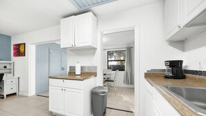 A modern kitchen with white cabinets, a coffee maker, and a dining area with a table and chairs. - Downtown Duplex- Spacious and Comfy 2 Bedroom (Gainesville)