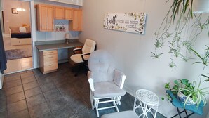 A compact kitchen with wooden cabinets, a dining area with a chair, and a wall-mounted sign. - Centrally located 2 bedroom condo for 6 people (Gainesville)