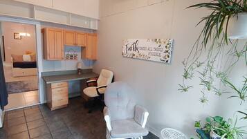 A compact kitchen with wooden cabinets, a dining area with a chair, and a wall-mounted sign.