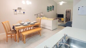 A modern living room with a dining area, a sofa, a TV, and a kitchen with a sink. - Centrally located 2 bedroom condo for 6 people (Gainesville)