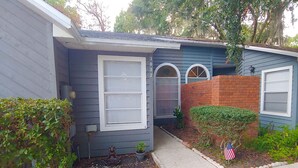 A single-story house with a front porch, a brick section, and a small garden area with a flag. - Centrally located 2 bedroom condo for 6 people (Gainesville)