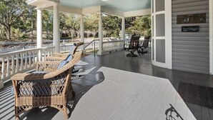 Eine überdachte Veranda mit Korbstühlen und einem Tisch, weißen Geländern und Blick auf Bäume.