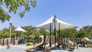 A playground with slides and climbing structures, surrounded by trees and covered by large umbrellas. - Location! Location!  Woodbury-Walking to Shopping and Activities 步行到商圈，活動中心 (Irvine)