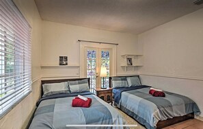 Un dormitorio con dos camas, una ventana con persianas, una puerta con vidrieras y una mesita de noche con lámpara.